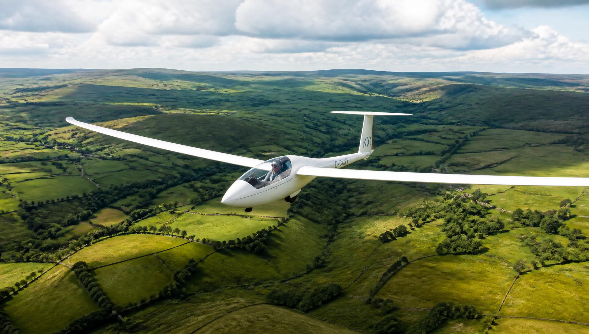 A single seat glider soaring above the patchwork fields of the Cotswolds on a summer afternoon