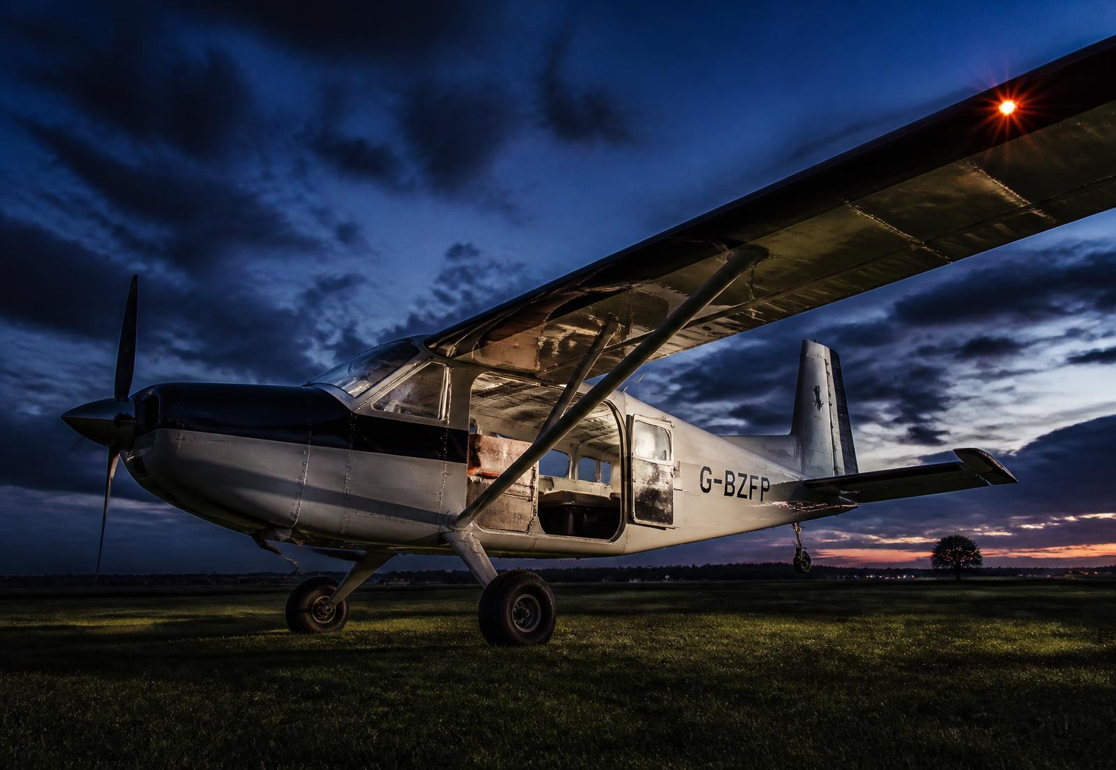A high wing single engine parachute operations aircraft on the grass at dusk