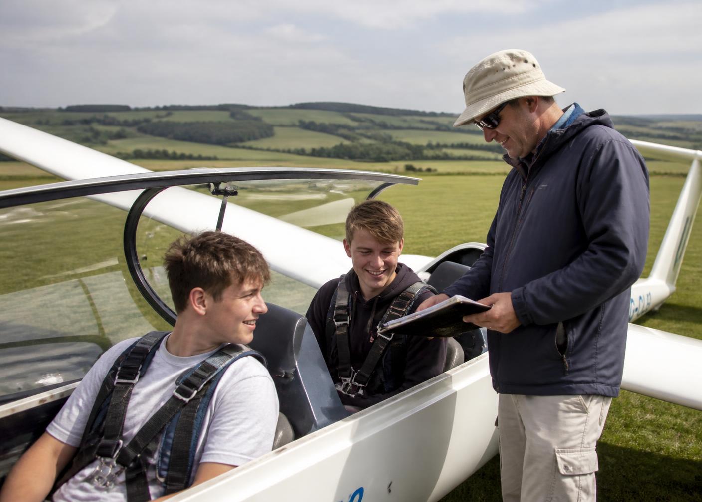 Young trainee pilots and an instructor briefing beside a glider on the grass at Vale Airfield